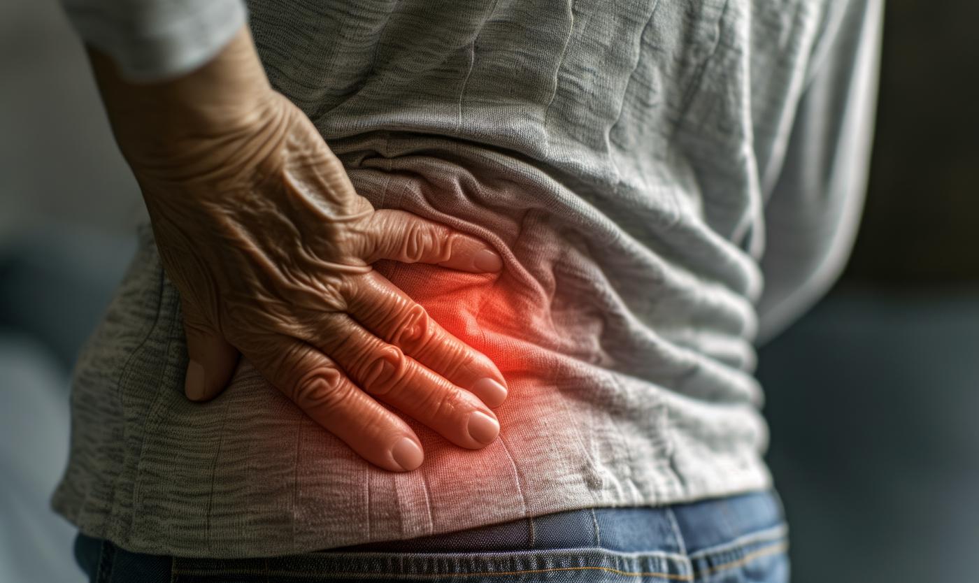 Close-up of the lower back and left side of a man holding his hand on his lower back from an attack of sharp pain, the concept of life insurance and injury ..